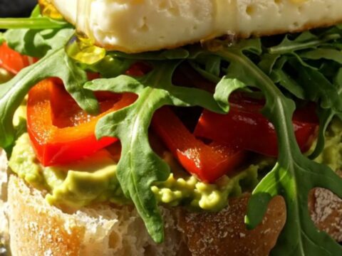 Close-up of a golden-seared halloumi sandwich on ciabatta with avocado and honey drizzle.