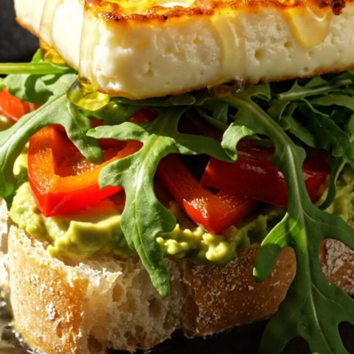 Close-up of a golden-seared halloumi sandwich on ciabatta with avocado and honey drizzle.