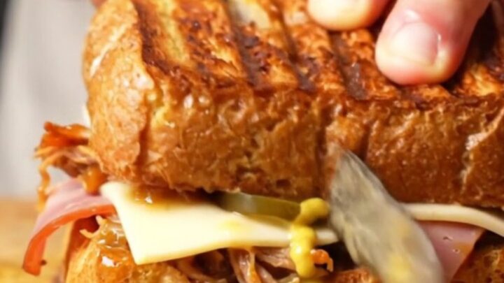 A close-up shot of a pressed Cuban medianoche sandwich with visible layers of pork, ham, and melted cheese.