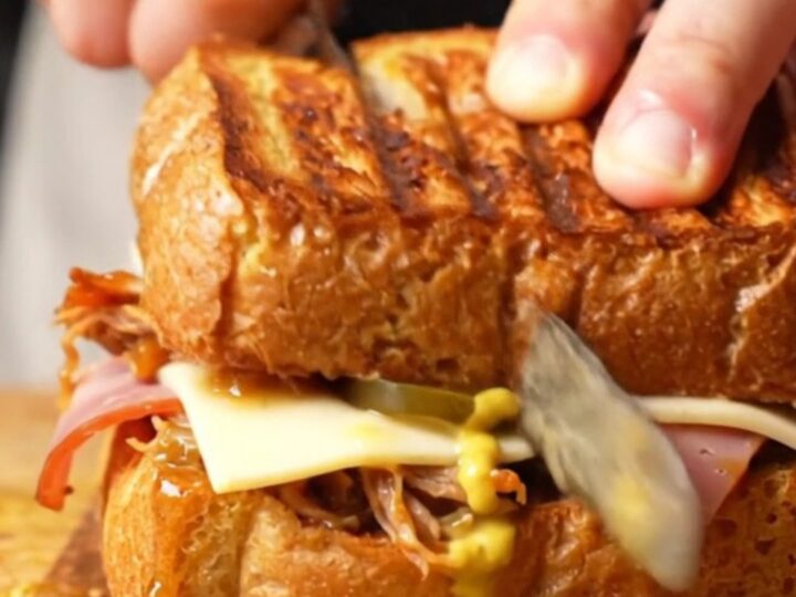 A close-up shot of a pressed Cuban medianoche sandwich with visible layers of pork, ham, and melted cheese.