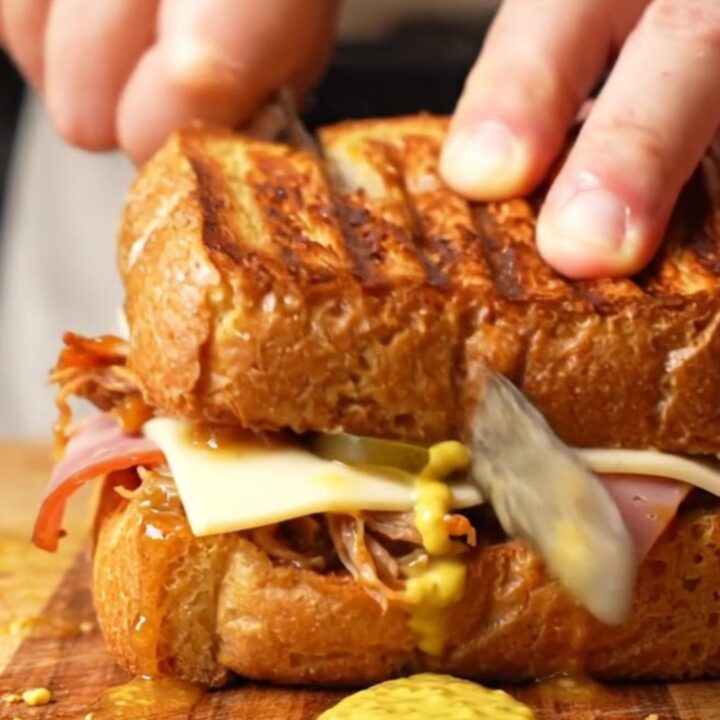 A close-up shot of a pressed Cuban medianoche sandwich with visible layers of pork, ham, and melted cheese.