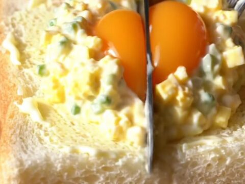 A close-up view of a Japanese Tamago Sando sandwich showing a creamy egg salad filling and a jammy egg center.