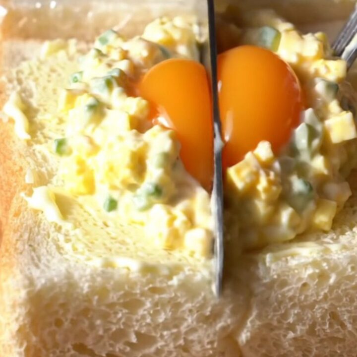 A close-up view of a Japanese Tamago Sando sandwich showing a creamy egg salad filling and a jammy egg center.