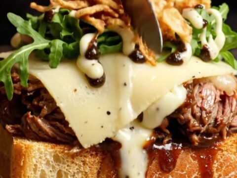 A gourmet braised beef cheek sandwich on a toasted brioche bun with melted Gruyère cheese and truffle aioli.