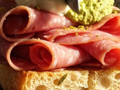 A close-up shot of a crispy rosemary focaccia sandwich overflowing with folded mortadella, creamy stracciatella cheese