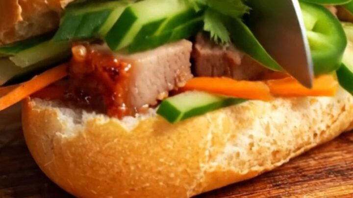 A close-up of a crispy Vietnamese Banh Mi sandwich filled with roast pork belly and fresh vegetables.