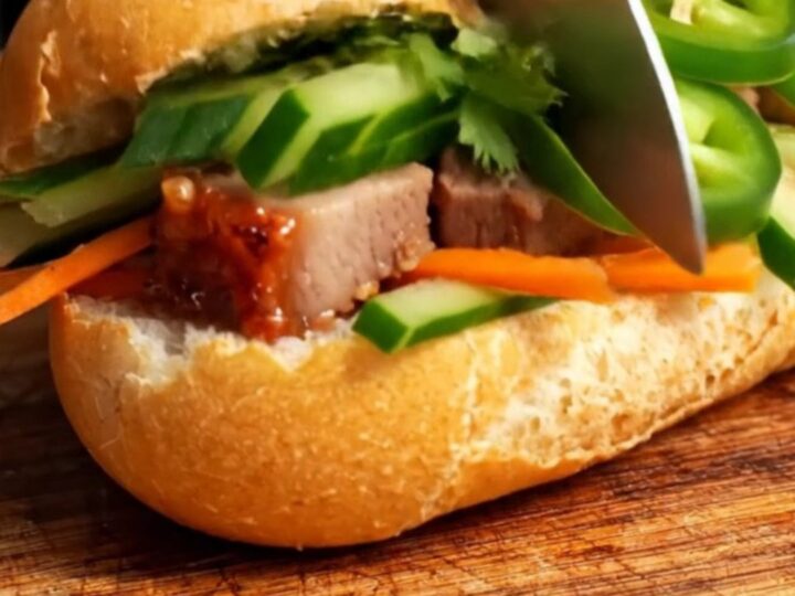 A close-up of a crispy Vietnamese Banh Mi sandwich filled with roast pork belly and fresh vegetables.