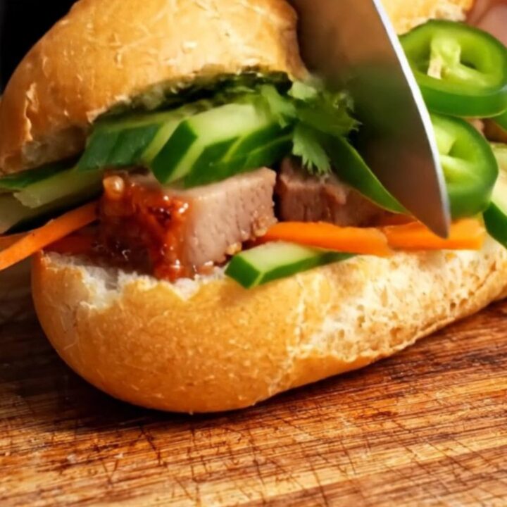 A close-up of a crispy Vietnamese Banh Mi sandwich filled with roast pork belly and fresh vegetables.