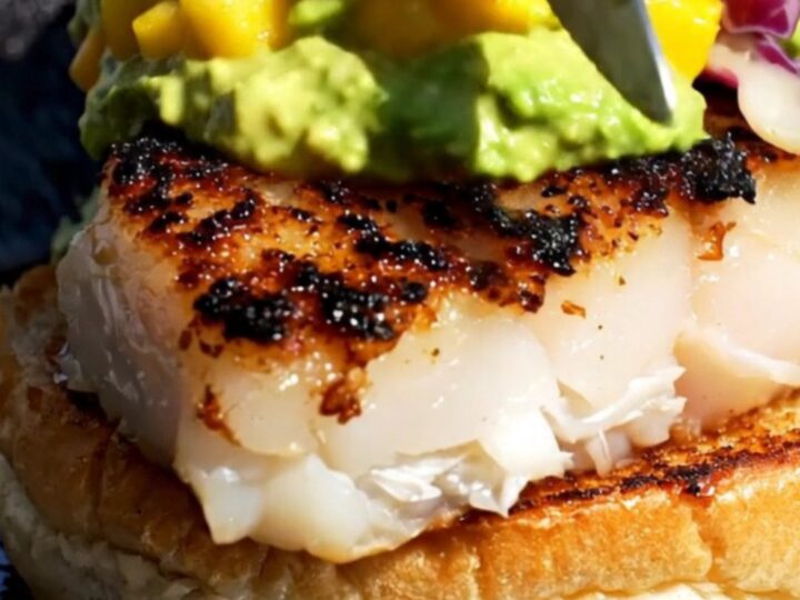 A close-up of a blackened mahi-mahi sandwich on a brioche bun with green avocado crema.