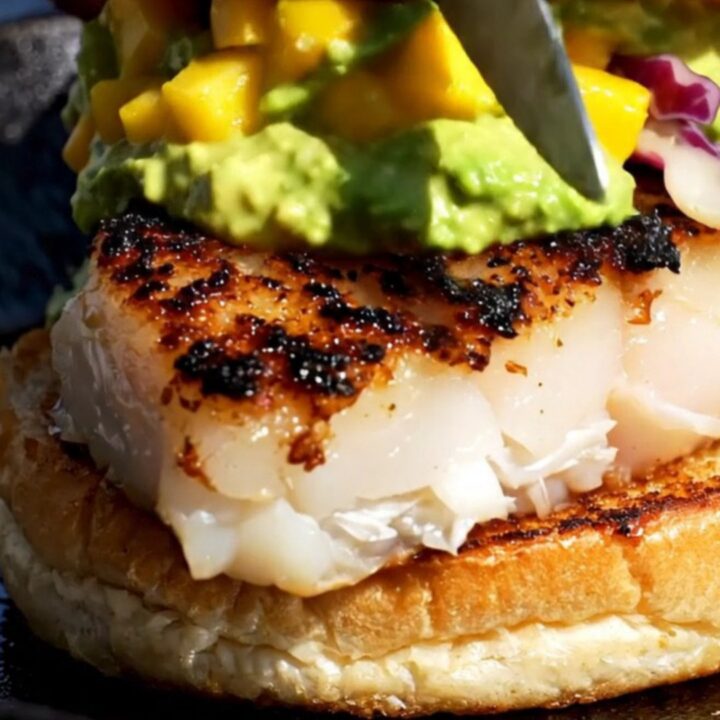 A close-up of a blackened mahi-mahi sandwich on a brioche bun with green avocado crema.