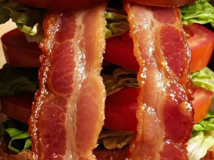 A close-up of a perfectly constructed sourdough BLT showing crispy bacon, vibrant tomato, and fresh lettuce.
