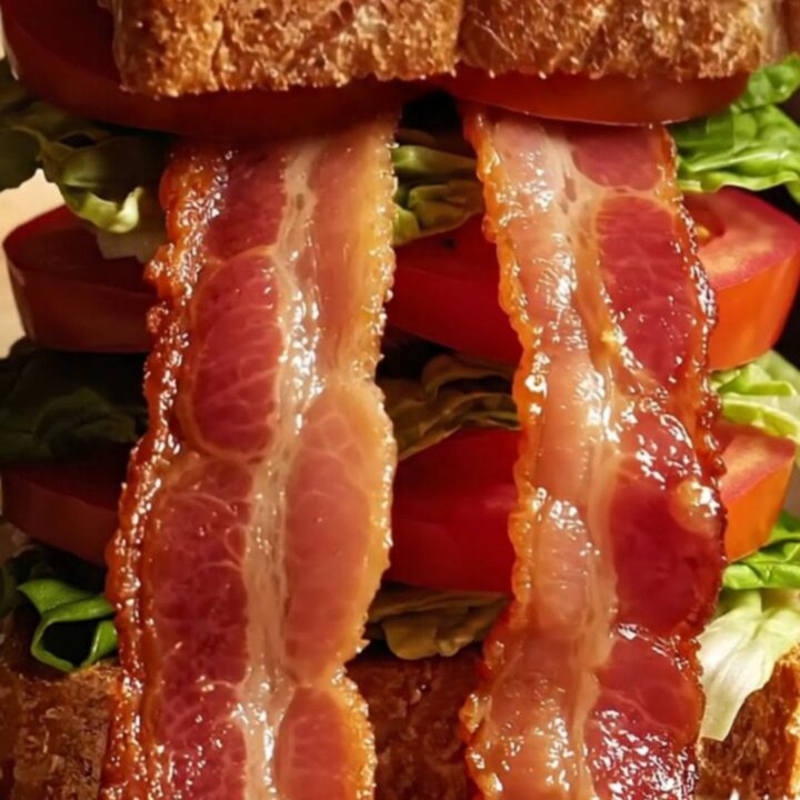 A close-up of a perfectly constructed sourdough BLT showing crispy bacon, vibrant tomato, and fresh lettuce.
