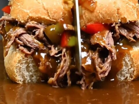 A close-up of a juicy Chicago Italian beef sandwich being dipped into a rich, steaming pot of beef gravy.