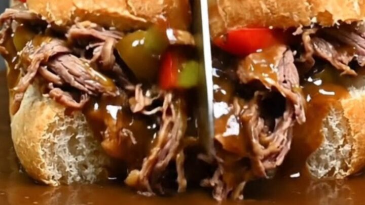 A close-up of a juicy Chicago Italian beef sandwich being dipped into a rich, steaming pot of beef gravy.