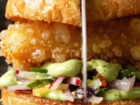 A close-up of a crispy tempura soft-shell crab sandwich on a toasted brioche bun with radish slaw.