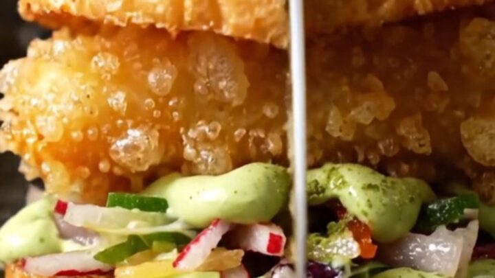 A close-up of a crispy tempura soft-shell crab sandwich on a toasted brioche bun with radish slaw.