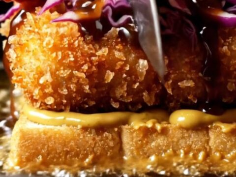A close-up view of a crispy tofu katsu sando on toasted milk bread with curry mayo.