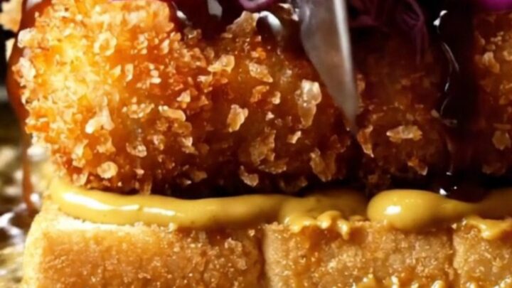 A close-up view of a crispy tofu katsu sando on toasted milk bread with curry mayo.