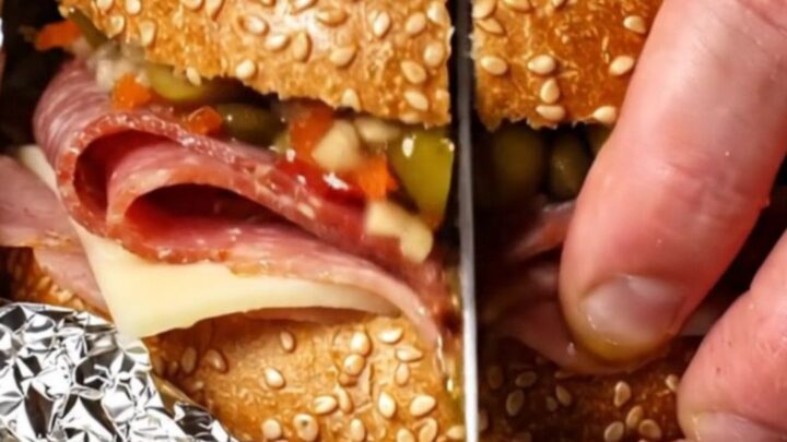 A close-up of a sliced New Orleans Muffuletta showing layers of salami, mortadella, ham, and cheese.