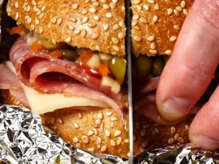A close-up of a sliced New Orleans Muffuletta showing layers of salami, mortadella, ham, and cheese.