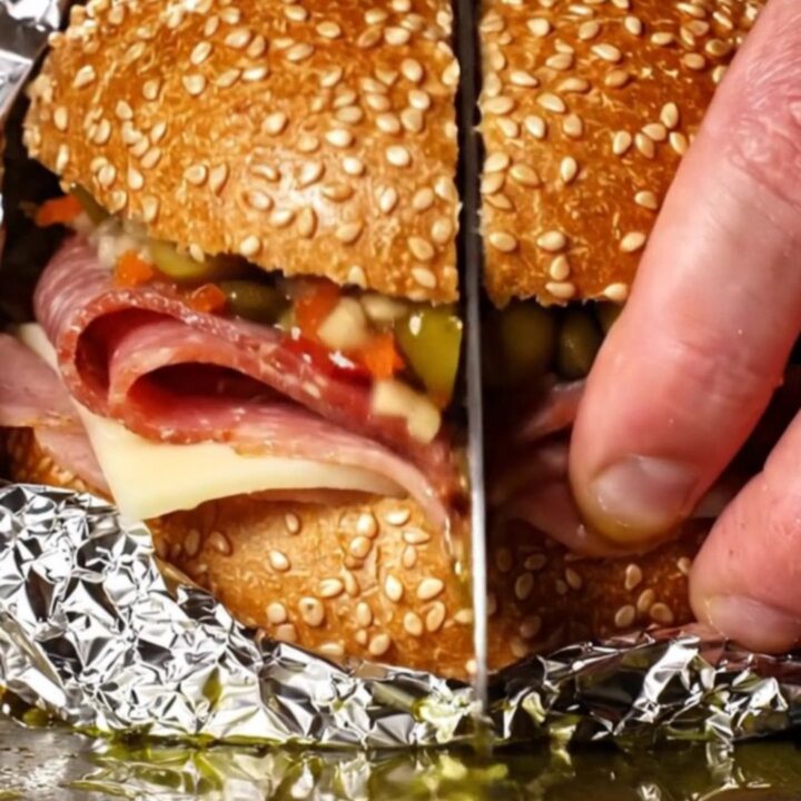 A close-up of a sliced New Orleans Muffuletta showing layers of salami, mortadella, ham, and cheese.