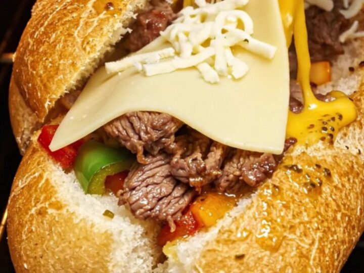 A crispy, golden-brown Philly cheesesteak stuffed garlic bread boat with a dramatic cheese pull.