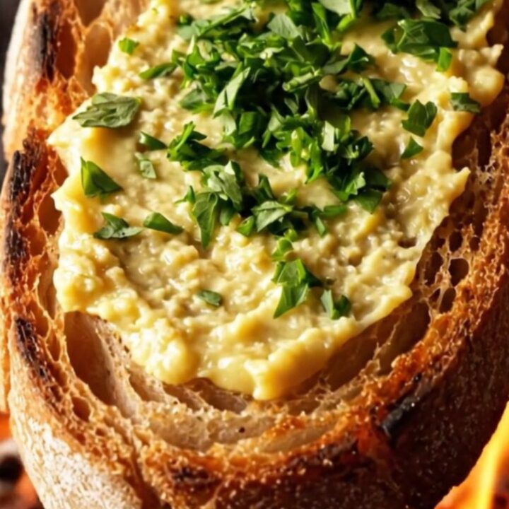 A close-up of a golden roasted bone marrow canoe with roasted garlic cloves on a piece of charred sourdough bread.