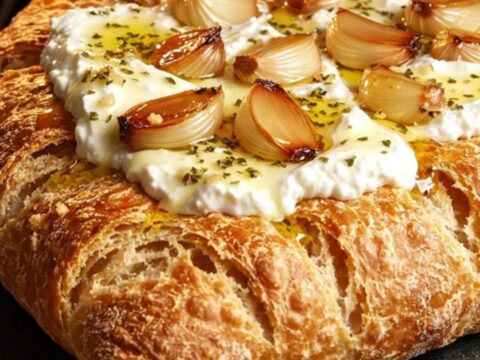 A close-up shot of crispy fougasse bread topped with fluffy whipped ricotta, roasted garlic cloves, and a drizzle of honey.