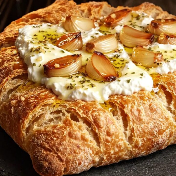 A close-up shot of crispy fougasse bread topped with fluffy whipped ricotta, roasted garlic cloves, and a drizzle of honey.