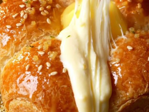 A close-up shot of a golden Korean cream cheese garlic bun with cream cheese oozing out of a pulled-apart wedge.