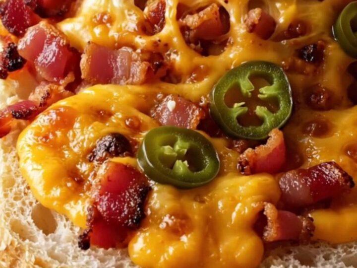 A close-up shot of a cheesy, golden jalapeño popper garlic bread with visible bacon and blistered cheese.