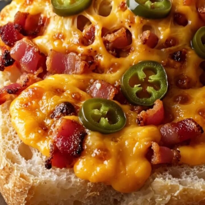 A close-up shot of a cheesy, golden jalapeño popper garlic bread with visible bacon and blistered cheese.