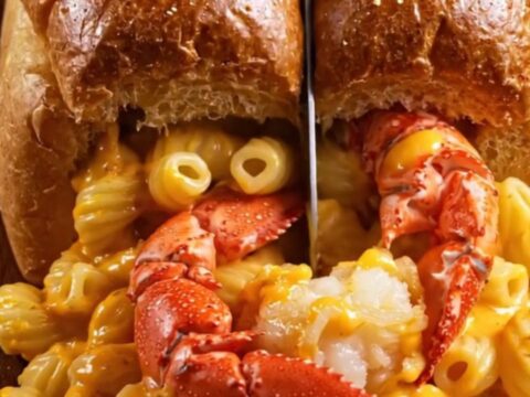 A golden-brown toasted brioche boat filled with creamy lobster mac and cheese, overflowing slightly.