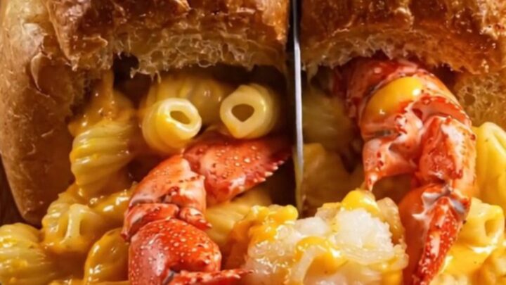A golden-brown toasted brioche boat filled with creamy lobster mac and cheese, overflowing slightly.
