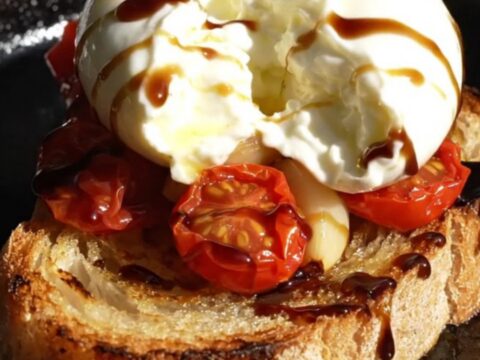 A close-up of golden-brown sourdough crostini topped with creamy burrata, burst cherry tomatoes, and fresh thyme.