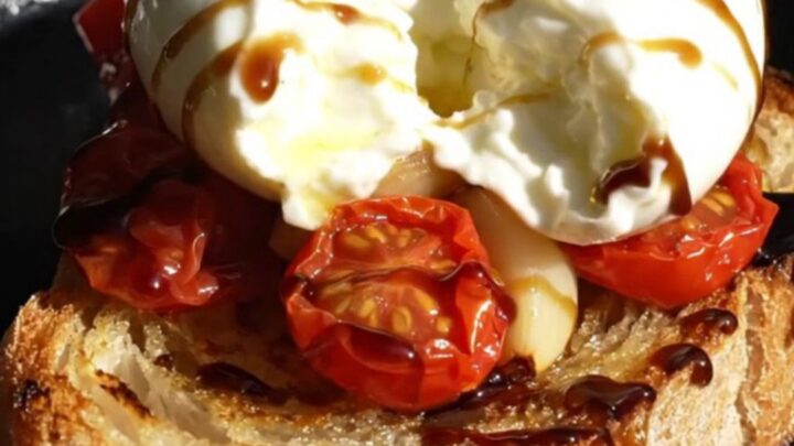 A close-up of golden-brown sourdough crostini topped with creamy burrata, burst cherry tomatoes, and fresh thyme.
