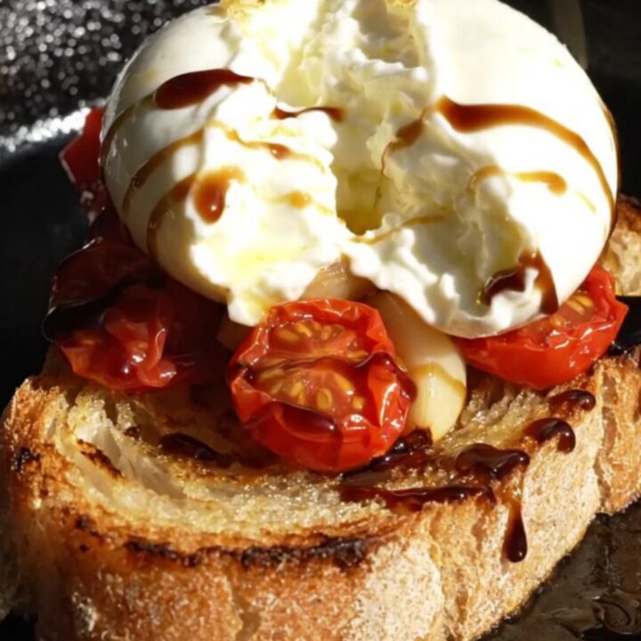 A close-up of golden-brown sourdough crostini topped with creamy burrata, burst cherry tomatoes, and fresh thyme.
