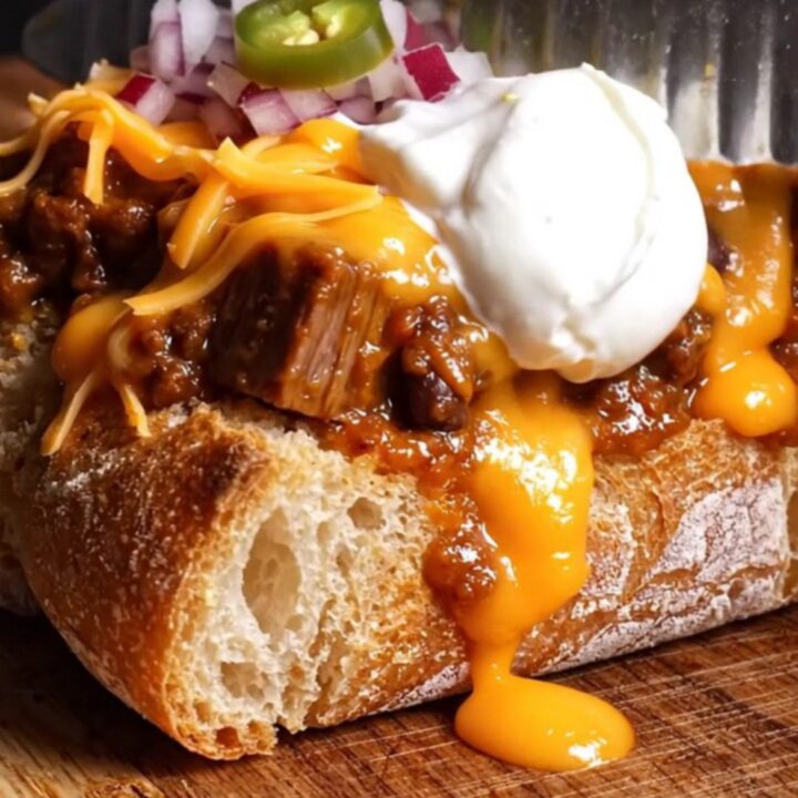 A crispy sourdough bread loaf hollowed out and filled with rich, dark smoked brisket chili and molten sharp cheddar cheese.