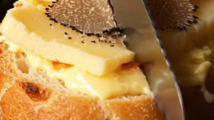 A close-up of golden-brown garlic bread topped with melted Taleggio and fresh shaved black truffles.