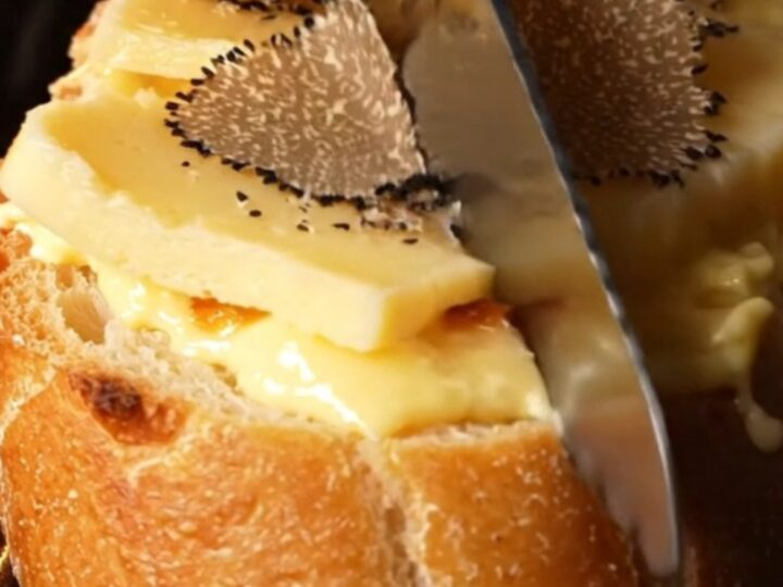A close-up of golden-brown garlic bread topped with melted Taleggio and fresh shaved black truffles.