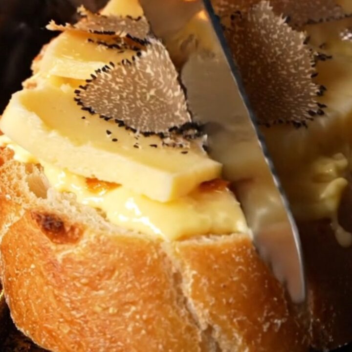 A close-up of golden-brown garlic bread topped with melted Taleggio and fresh shaved black truffles.