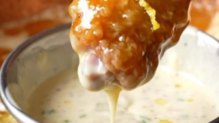 A close-up of golden-brown fried chicken wings coated in a glossy, amber hot honey glaze with lemon zest.