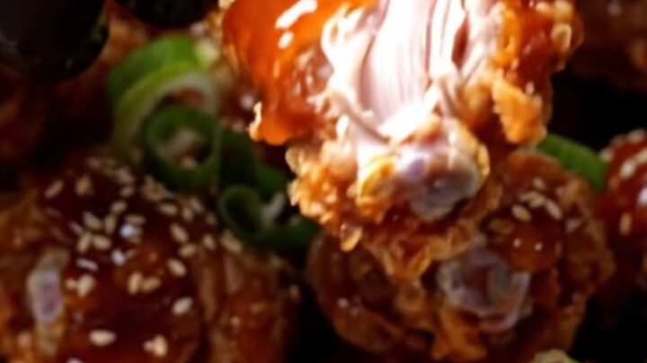 Cinematic close-up of crispy Korean wings glistening with a vibrant red gochujang glaze and sesame seeds.
