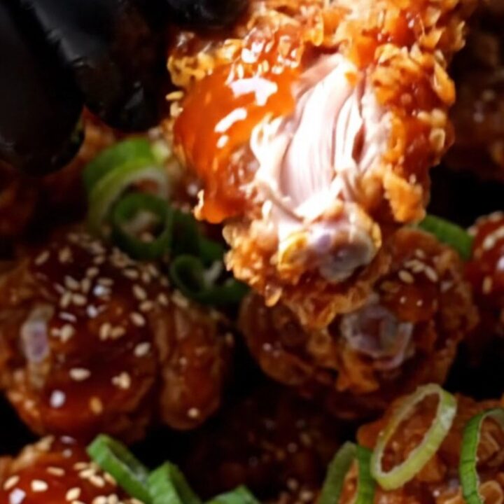 Cinematic close-up of crispy Korean wings glistening with a vibrant red gochujang glaze and sesame seeds.
