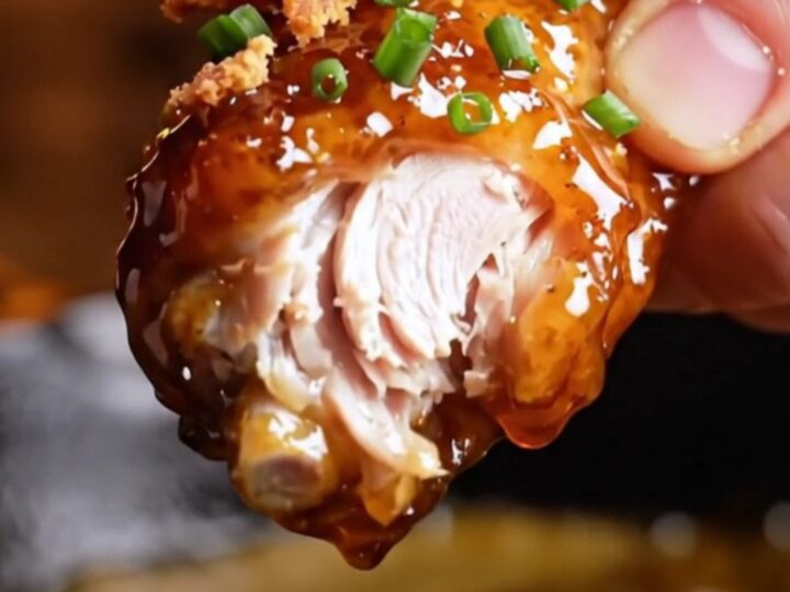 A close-up shot of crispy chicken wings coated in a shiny, dark mahogany chipotle maple bourbon glaze.