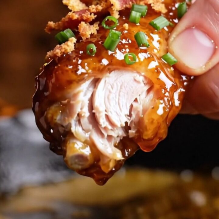 A close-up shot of crispy chicken wings coated in a shiny, dark mahogany chipotle maple bourbon glaze.
