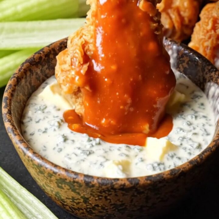 A close-up of crispy double-fried chicken wings coated in vibrant orange buffalo sauce with blue cheese crumbles.