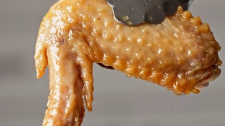 A golden, crispy bone-in chicken wing tossed in a dark wok with sliced red chilies and garlic.
