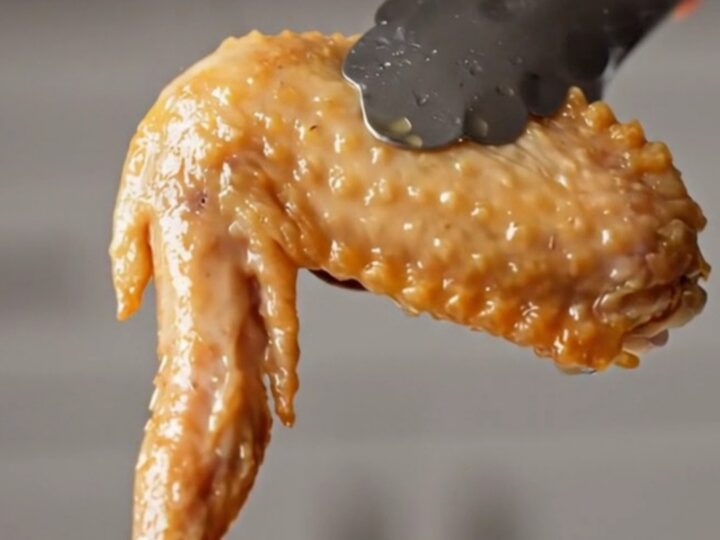 A golden, crispy bone-in chicken wing tossed in a dark wok with sliced red chilies and garlic.