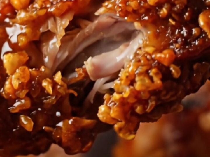 A close-up of crispy, charred Jamaican jerk chicken wings on a cast-iron pan with a glossy glaze.